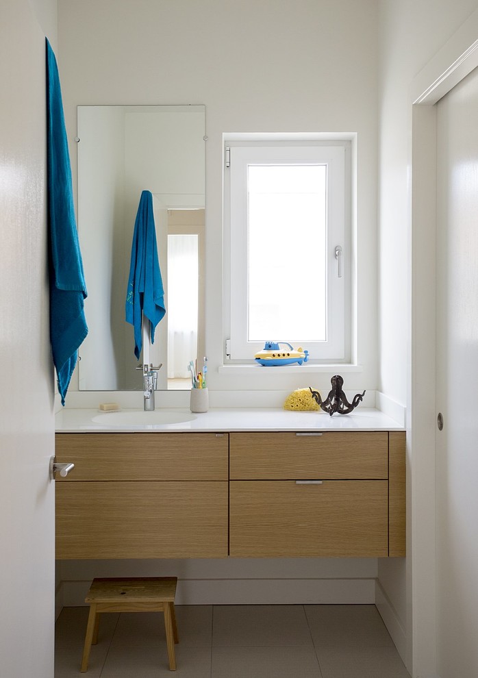 Diseño de cuarto de baño infantil contemporáneo con armarios con paneles lisos, paredes blancas, suelo de baldosas de porcelana, lavabo integrado, encimera de acrílico y puertas de armario de madera clara