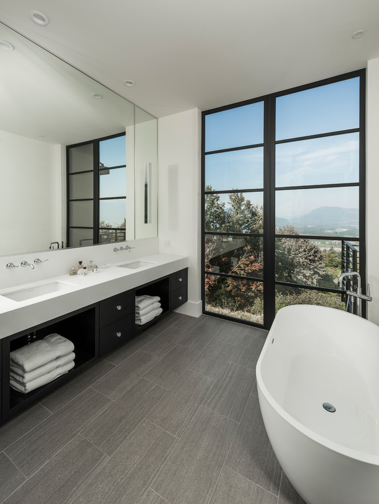 Стильный дизайн: большая главная ванная комната в современном стиле с плоскими фасадами, черными фасадами, отдельно стоящей ванной, белыми стенами, полом из керамогранита, врезной раковиной, серым полом и белой столешницей - последний тренд