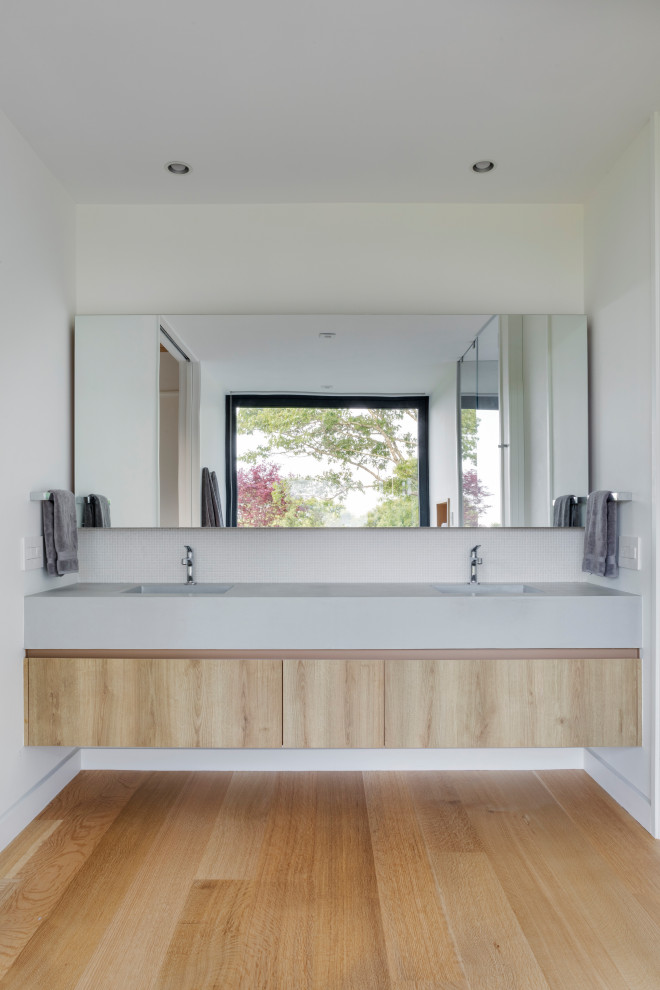 Exemple d'une grande salle de bain principale tendance en bois brun avec un placard à porte plane, un carrelage blanc, un mur blanc, un sol en bois brun, un sol beige, un plan de toilette blanc, meuble double vasque et meuble-lavabo suspendu.