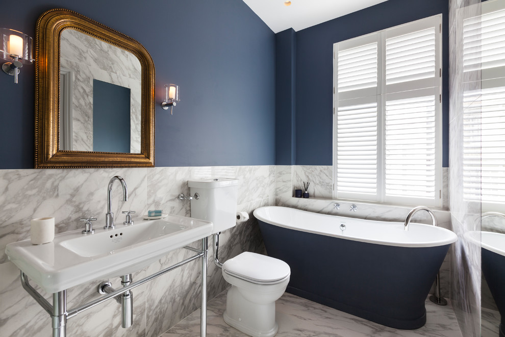 На фото: главная ванная комната среднего размера в стиле неоклассика (современная классика) с отдельно стоящей ванной, раздельным унитазом, белой плиткой, синими стенами, мраморным полом, консольной раковиной, белым полом, мраморной плиткой и зеркалом с подсветкой с
