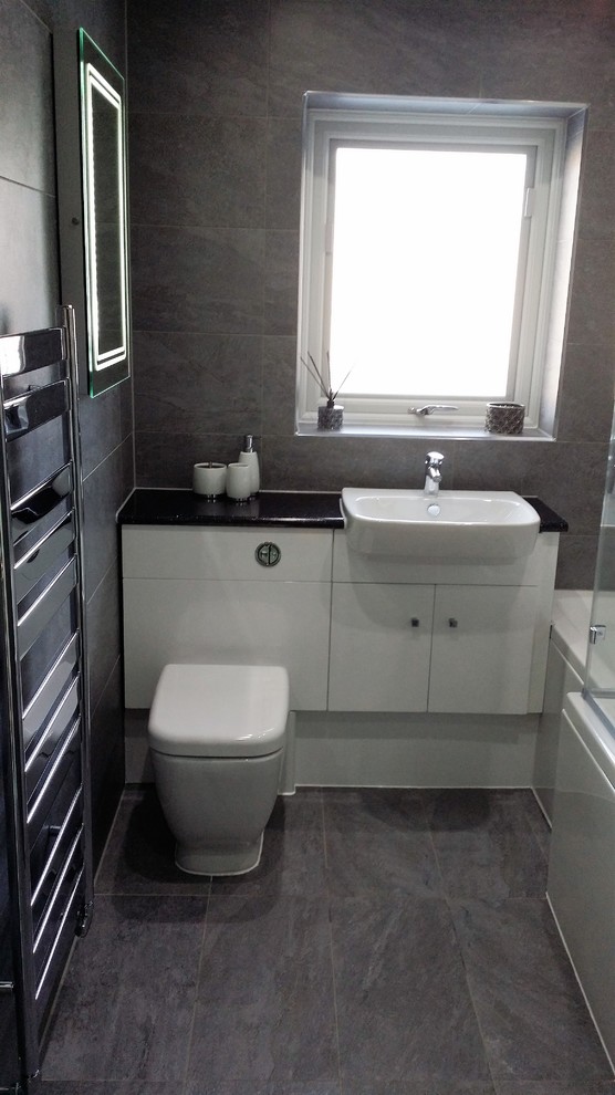This is an example of a medium sized contemporary family bathroom in Cheshire with flat-panel cabinets, white cabinets, an alcove bath, a one-piece toilet, grey tiles, porcelain tiles, grey walls, porcelain flooring, a built-in sink and laminate worktops.
