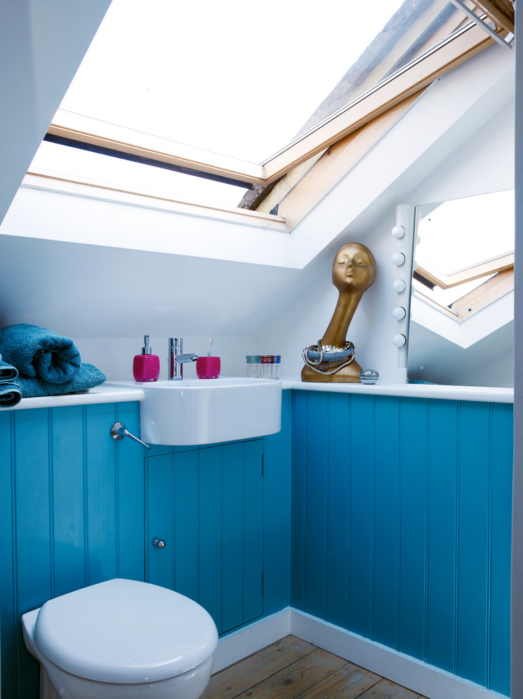 Modern inredning av ett litet badrum, med ett väggmonterat handfat, blå skåp, en vägghängd toalettstol, vita väggar och mellanmörkt trägolv