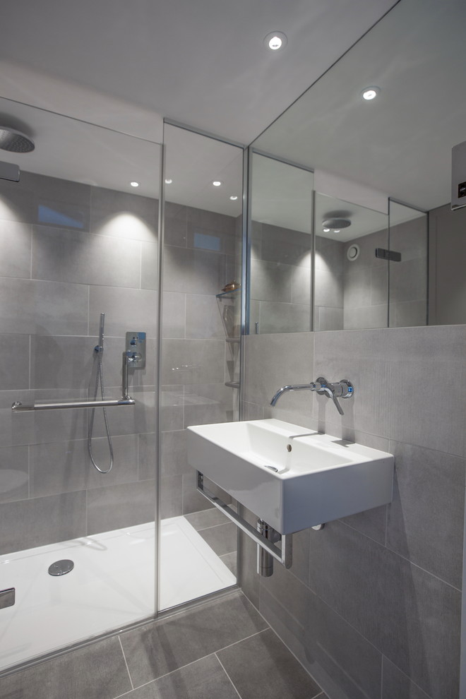 Industriell inredning av ett mellanstort badrum med dusch, med en kantlös dusch, en vägghängd toalettstol, grå kakel, keramikplattor, grå väggar, klinkergolv i keramik, ett väggmonterat handfat och marmorbänkskiva