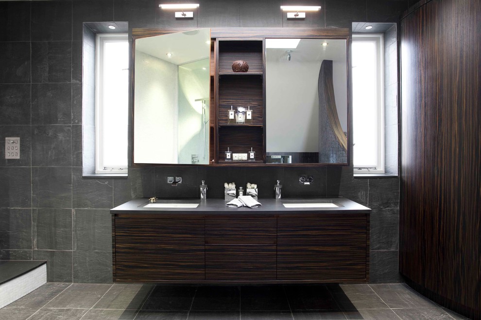 Exemple d'une salle de bain principale tendance en bois foncé de taille moyenne avec un lavabo encastré, un placard à porte plane, un carrelage noir, un mur noir, un plan de toilette en surface solide, une baignoire indépendante, WC à poser, mosaïque et un sol en carrelage de porcelaine.