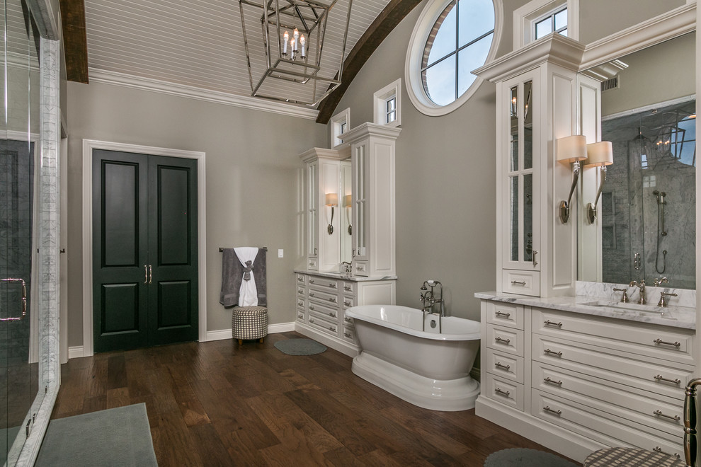 Inspiration for a large transitional master white tile and marble tile medium tone wood floor and brown floor bathroom remodel in Dallas with raised-panel cabinets, white cabinets, a one-piece toilet, gray walls, an undermount sink, marble countertops and a hinged shower door