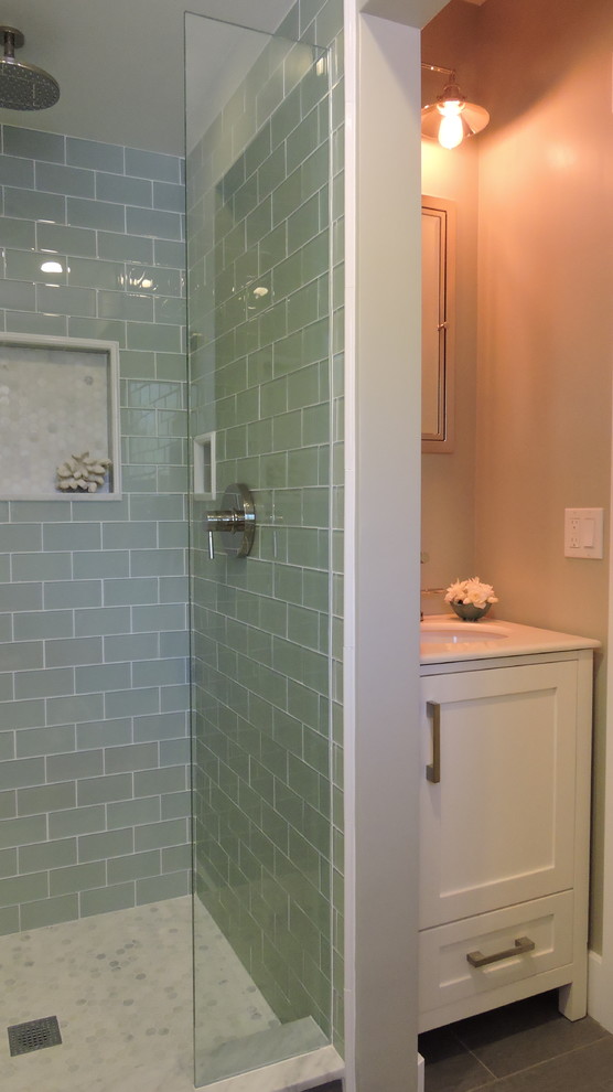 Bild på ett litet maritimt badrum med dusch, med ett undermonterad handfat, möbel-liknande, vita skåp, marmorbänkskiva, en dusch i en alkov, vit kakel, glaskakel, beige väggar och kalkstensgolv