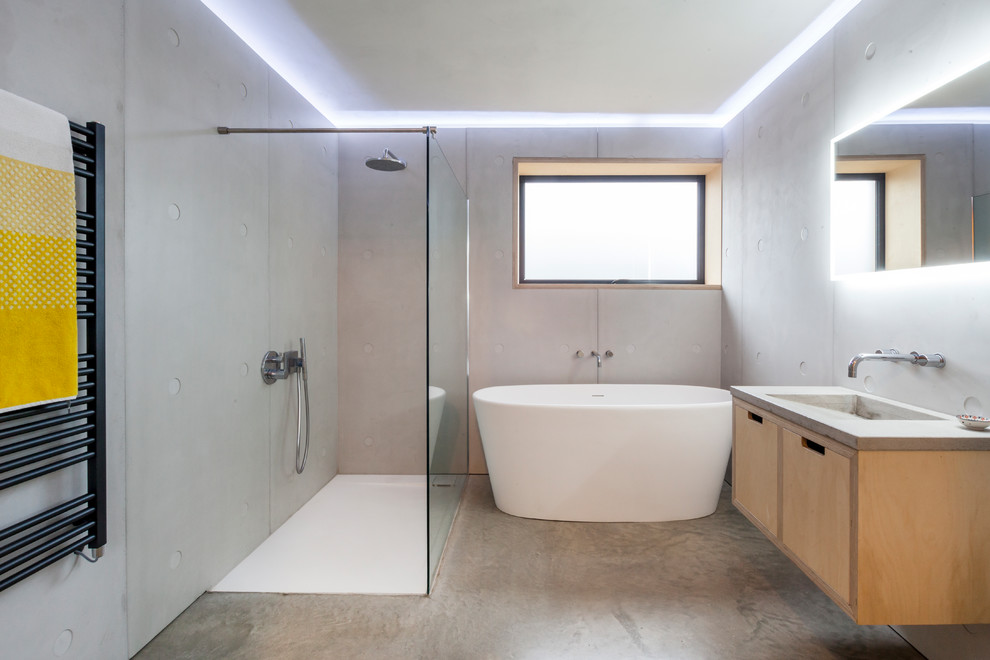 На фото: главная ванная комната среднего размера в стиле модернизм с плоскими фасадами, светлыми деревянными фасадами, отдельно стоящей ванной, открытым душем, серыми стенами, бетонным полом, столешницей из бетона, серым полом, серой плиткой, монолитной раковиной и открытым душем с