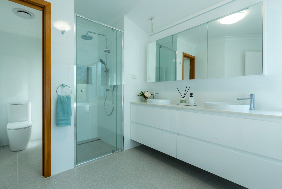 Свежая идея для дизайна: большая главная ванная комната в стиле модернизм с плоскими фасадами, белыми фасадами, отдельно стоящей ванной, душем в нише, унитазом-моноблоком, белой плиткой, керамической плиткой, белыми стенами, полом из керамогранита, настольной раковиной, столешницей из искусственного кварца, разноцветным полом, душем с распашными дверями, белой столешницей, тумбой под две раковины и подвесной тумбой - отличное фото интерьера