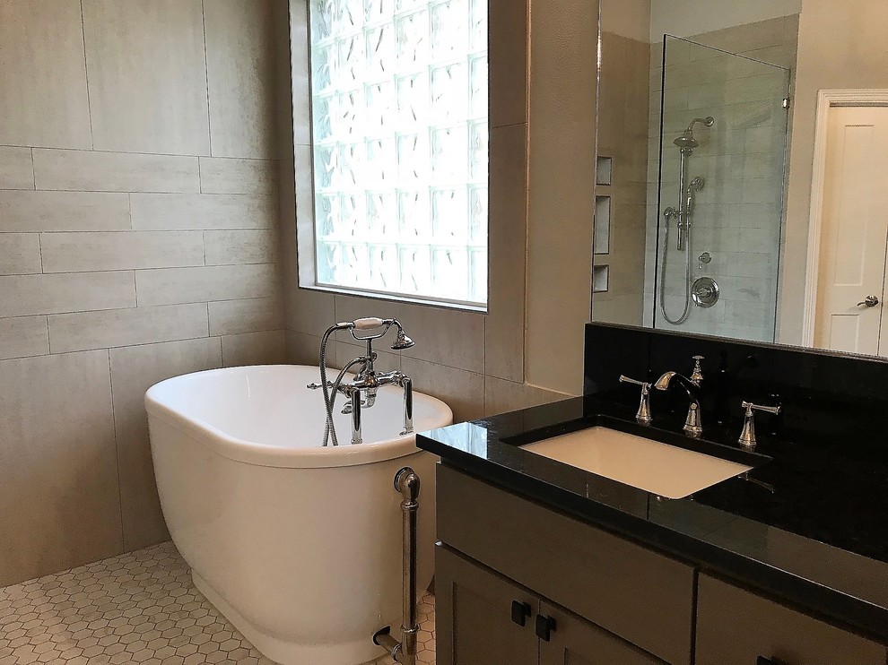 Exemple d'une grande salle de bain principale chic avec un placard à porte shaker, des portes de placard grises, un sol en marbre, un plan de toilette en marbre, une baignoire indépendante, un espace douche bain, des carreaux de porcelaine, un mur gris, un lavabo encastré, aucune cabine et un plan de toilette noir.