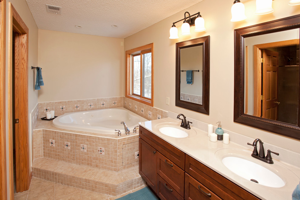 Cette photo montre une salle de bain chic en bois brun avec un lavabo encastré, un placard avec porte à panneau encastré, une baignoire d'angle, un carrelage beige et des carreaux de céramique.
