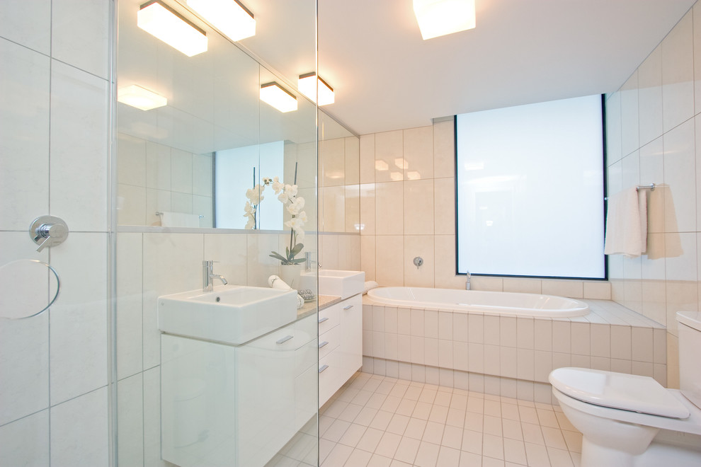 Inredning av ett modernt mellanstort en-suite badrum, med släta luckor, vita skåp, ett platsbyggt badkar, en hörndusch, en toalettstol med separat cisternkåpa, vit kakel, vita väggar, ett fristående handfat, vitt golv och dusch med gångjärnsdörr