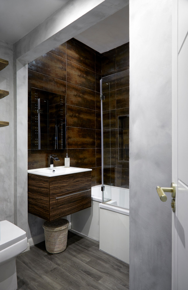 Inspiration för ett litet industriellt brun brunt badrum, med släta luckor, bruna skåp, ett platsbyggt badkar, en dusch/badkar-kombination, en toalettstol med hel cisternkåpa, brun kakel, keramikplattor, grå väggar, vinylgolv, ett väggmonterat handfat, träbänkskiva, grått golv och dusch med gångjärnsdörr