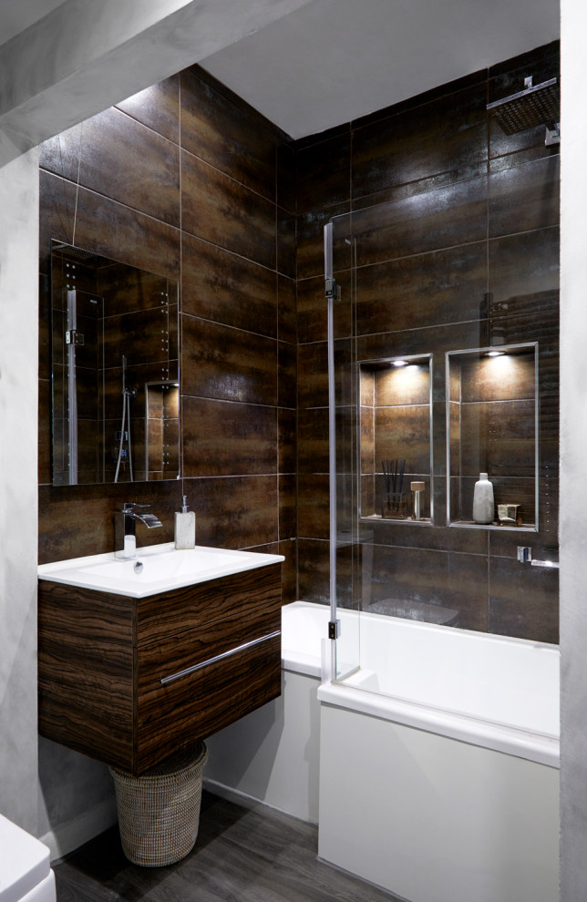 Bild på ett litet industriellt brun brunt badrum, med släta luckor, bruna skåp, ett platsbyggt badkar, en dusch/badkar-kombination, en toalettstol med hel cisternkåpa, brun kakel, keramikplattor, grå väggar, vinylgolv, ett väggmonterat handfat, träbänkskiva, grått golv och dusch med gångjärnsdörr