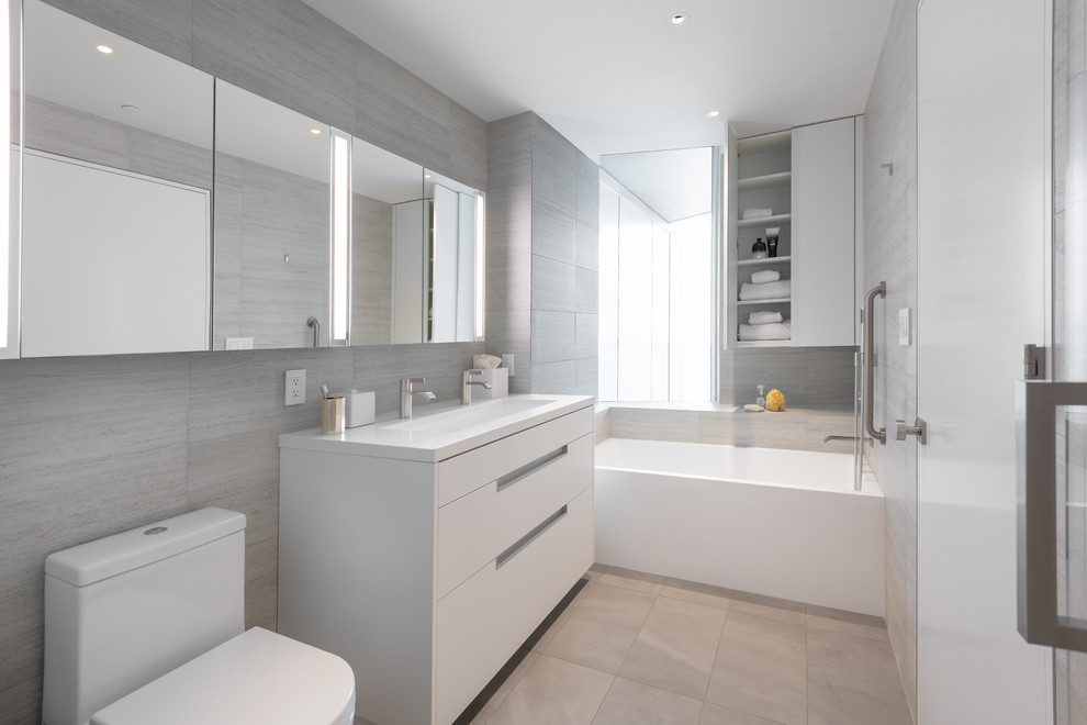 Cette image montre une salle de bain principale design avec des portes de placard blanches, une baignoire posée, une douche double, un carrelage gris, un mur beige, une grande vasque, un sol gris et un plan de toilette blanc.