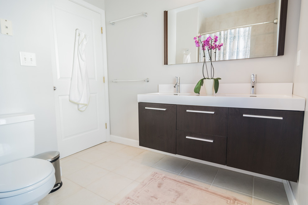 Mid-sized trendy master beige tile and ceramic tile ceramic tile and beige floor bathroom photo in Boston with flat-panel cabinets, dark wood cabinets, a two-piece toilet, gray walls, an integrated sink and solid surface countertops