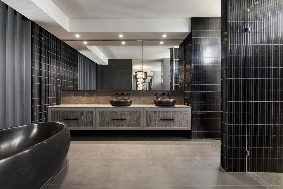 Design ideas for a contemporary ensuite bathroom in Melbourne with flat-panel cabinets, grey cabinets, a freestanding bath, black tiles, a vessel sink and a hinged door.
