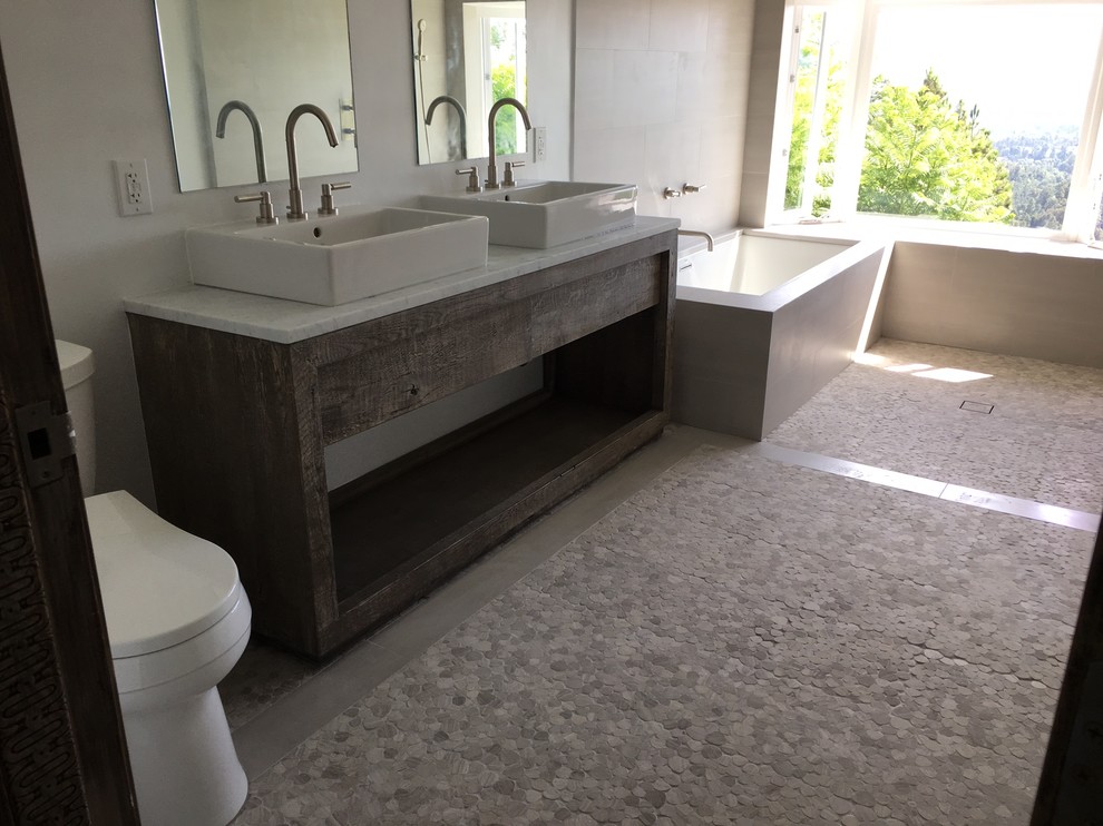Cette image montre une salle de bain principale chalet de taille moyenne avec une baignoire d'angle, un espace douche bain, un carrelage gris, des carreaux de porcelaine et un plan de toilette en marbre.