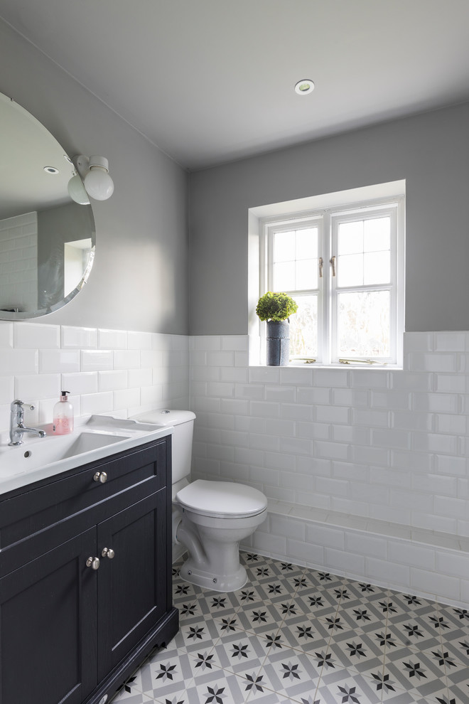 Photo of a medium sized contemporary ensuite bathroom in Surrey with freestanding cabinets, grey cabinets, a walk-in shower, a wall mounted toilet, white tiles, metro tiles, grey walls, ceramic flooring, a pedestal sink, solid surface worktops, grey floors, an open shower and white worktops.
