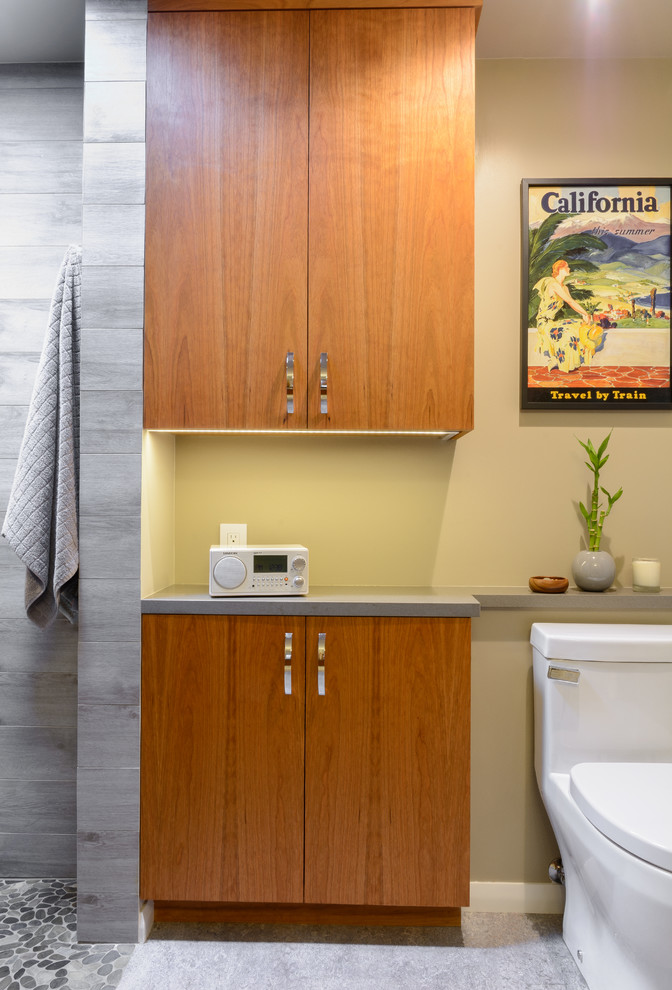 Mid-sized trendy master gray tile and porcelain tile pebble tile floor doorless shower photo in Los Angeles with flat-panel cabinets, medium tone wood cabinets, a one-piece toilet, gray walls, an undermount sink and quartz countertops