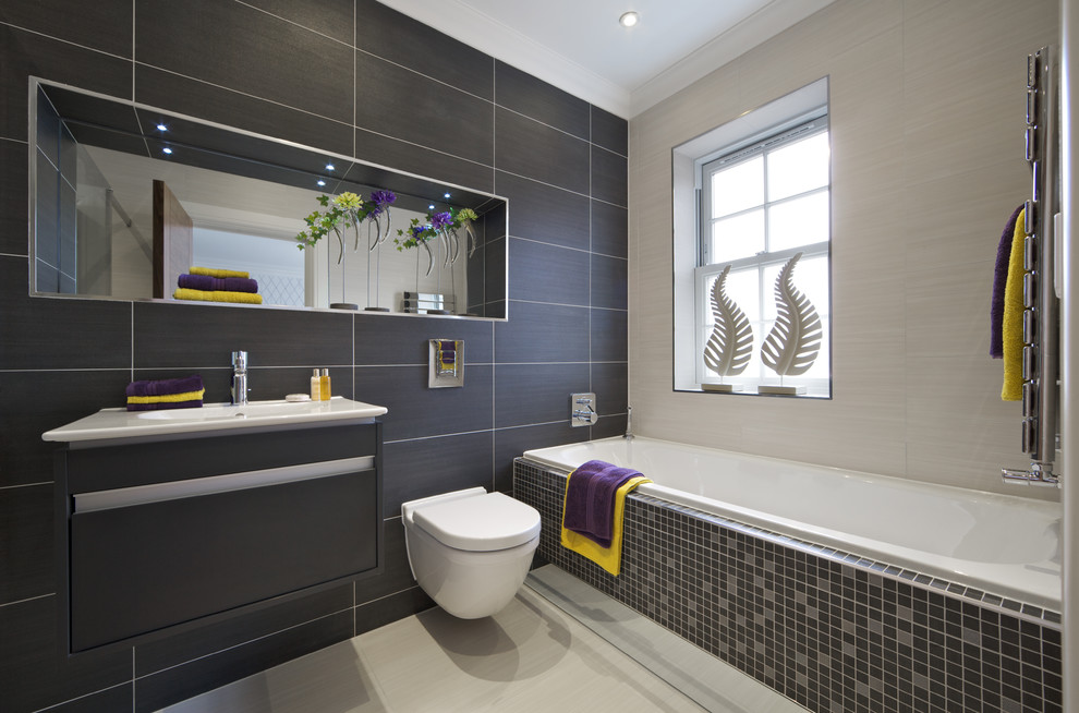 Idee per una stanza da bagno minimal con lavabo integrato, ante lisce, ante grigie, vasca da incasso, WC sospeso, piastrelle grigie e piastrelle in gres porcellanato