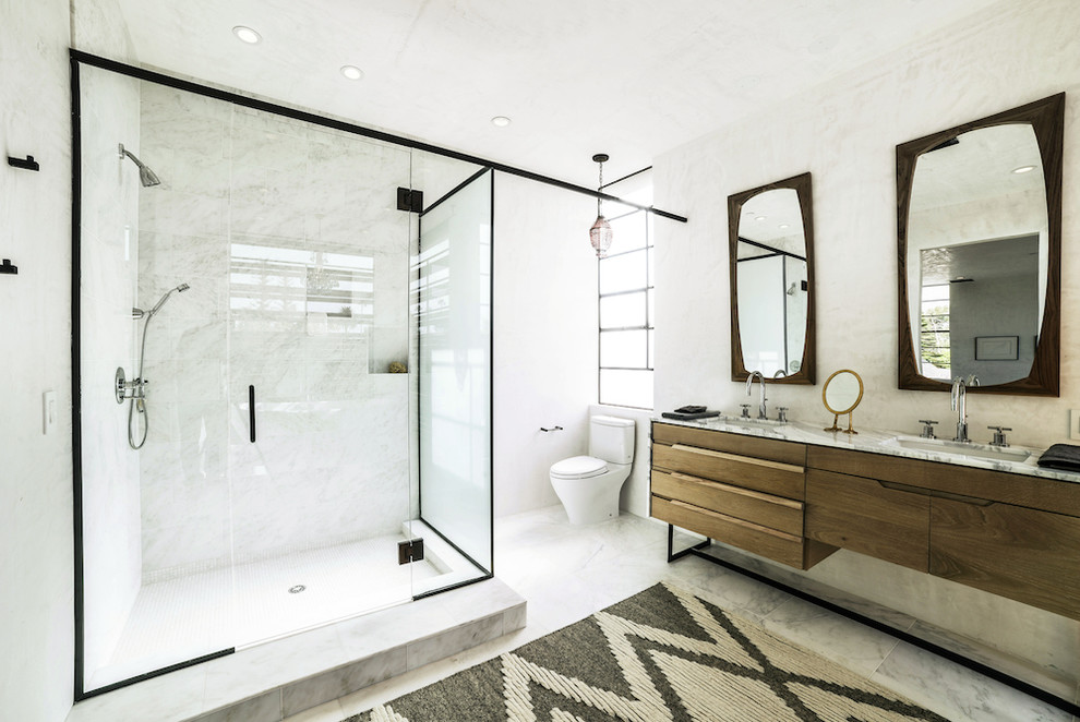 Modelo de cuarto de baño principal de tamaño medio con puertas de armario de madera oscura, bañera exenta, ducha esquinera, paredes blancas y suelo de baldosas de porcelana