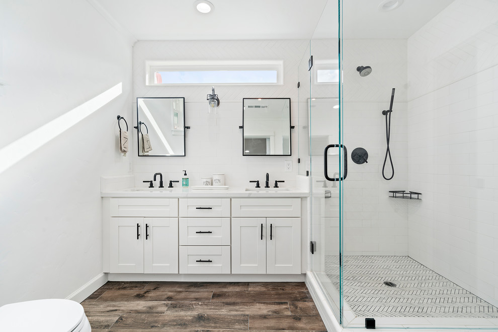 Bild på ett lantligt vit vitt badrum med dusch, med skåp i shakerstil, vita skåp, en hörndusch, vit kakel, vita väggar, mellanmörkt trägolv, ett undermonterad handfat, brunt golv och dusch med gångjärnsdörr