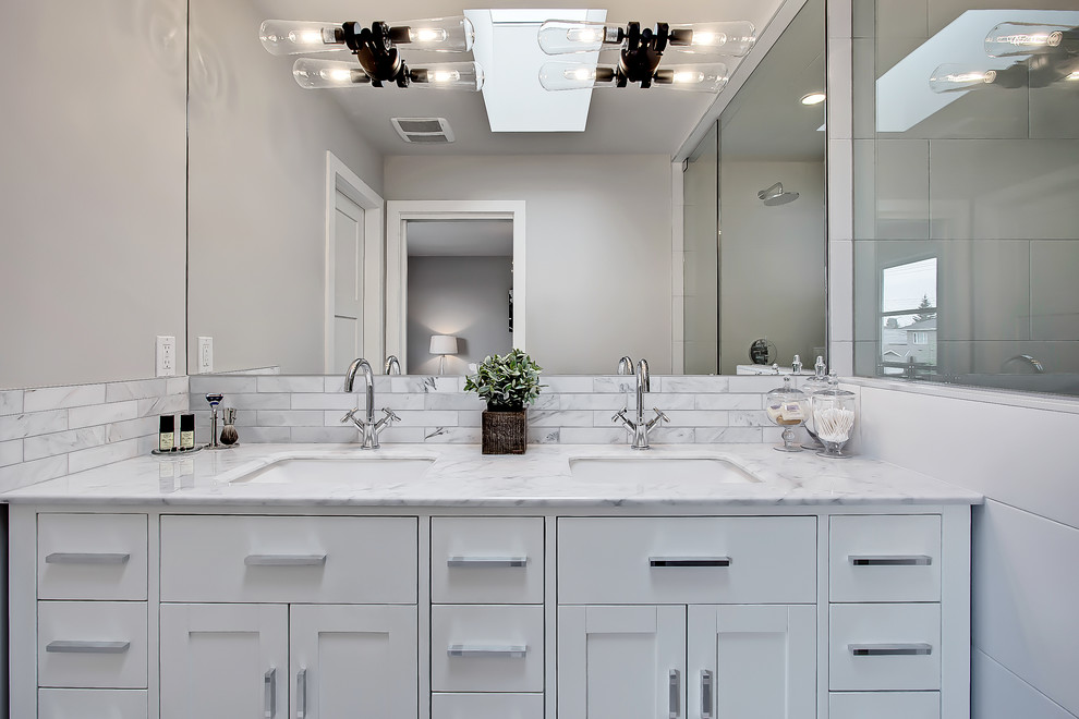 Example of a mid-sized transitional master white tile and ceramic tile porcelain tile and white floor walk-in shower design in Calgary with shaker cabinets, white cabinets, a two-piece toilet, gray walls, an undermount sink, marble countertops and a hinged shower door