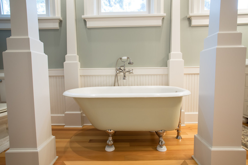 Inredning av ett klassiskt stort en-suite badrum, med luckor med profilerade fronter, vita skåp, ett badkar med tassar, en toalettstol med separat cisternkåpa, gröna väggar, mellanmörkt trägolv, ett undermonterad handfat, marmorbänkskiva och brunt golv