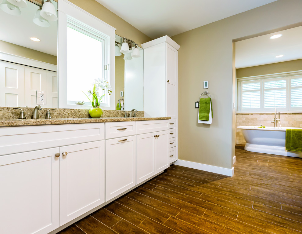 This is an example of a medium sized traditional ensuite bathroom in Detroit with a submerged sink, shaker cabinets, white cabinets, a freestanding bath, an alcove shower, a one-piece toilet, beige tiles, travertine tiles, beige walls, dark hardwood flooring, granite worktops, brown floors and a hinged door.