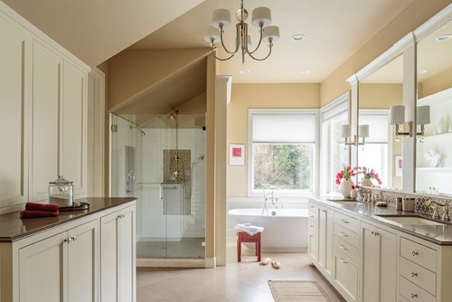 Elegant bathroom with cream-colored cabinets, glass shower, soaking tub, and double vanity with marble countertops.