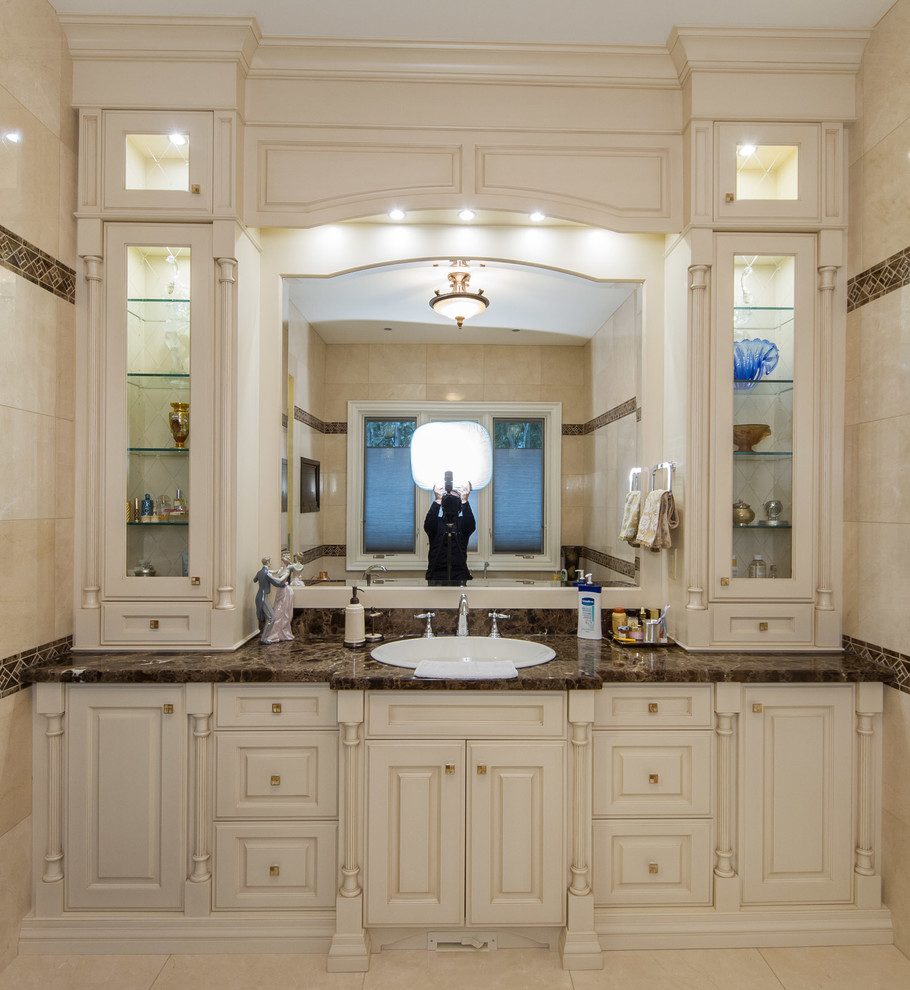 Idée de décoration pour une salle d'eau tradition de taille moyenne avec un plan vasque, un placard avec porte à panneau surélevé, des portes de placard beiges, un plan de toilette en granite, un carrelage beige, des carreaux de céramique et un mur beige.