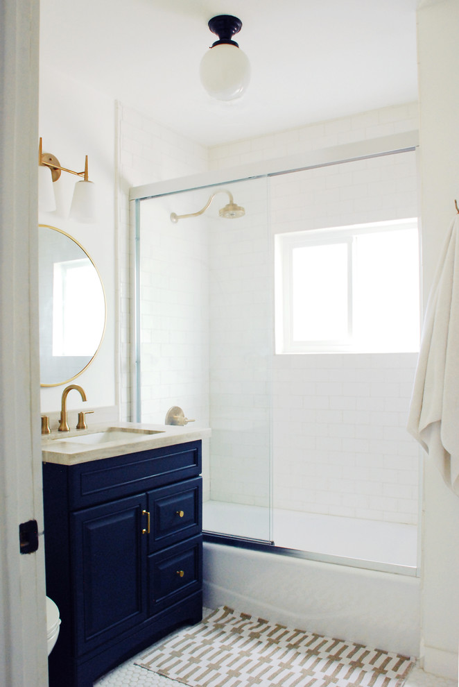 Стильный дизайн: маленькая ванная комната в стиле неоклассика (современная классика) с синими фасадами, ванной в нише, душем над ванной, белой плиткой, керамической плиткой, белыми стенами, полом из керамической плитки, врезной раковиной, столешницей из известняка, белым полом и душем с раздвижными дверями для на участке и в саду - последний тренд