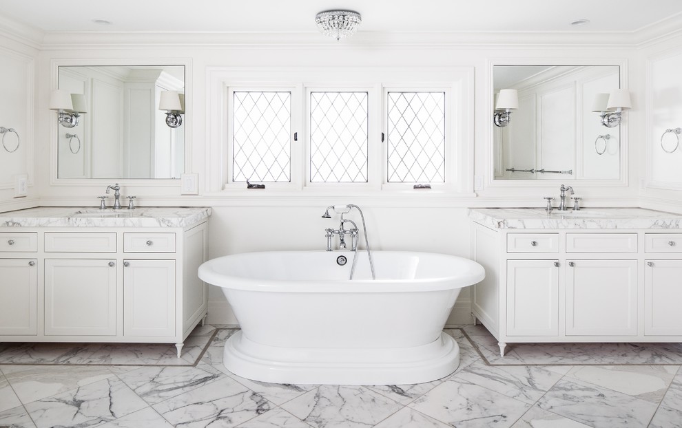 Aménagement d'une salle d'eau classique avec un placard à porte shaker, des portes de placard blanches, une baignoire indépendante, un mur blanc, un sol en marbre, un lavabo encastré, un sol blanc et un plan de toilette blanc.