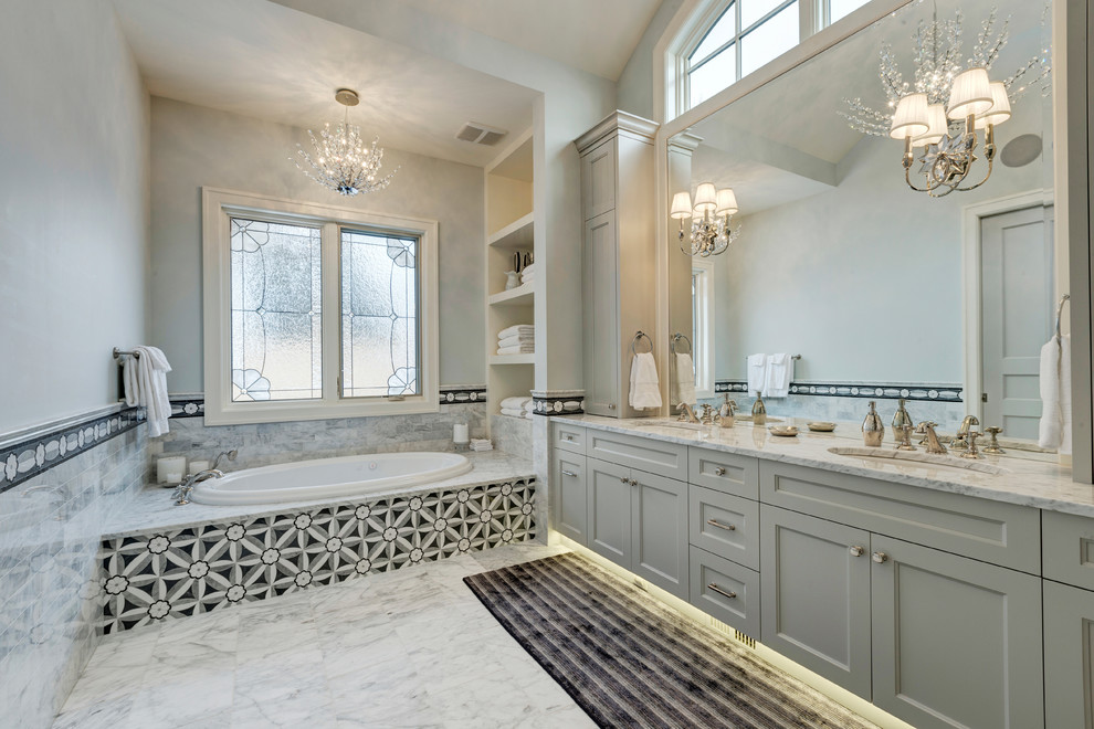 Klassisk inredning av ett badrum, med ett undermonterad handfat, luckor med infälld panel, grå skåp, ett platsbyggt badkar och grå väggar
