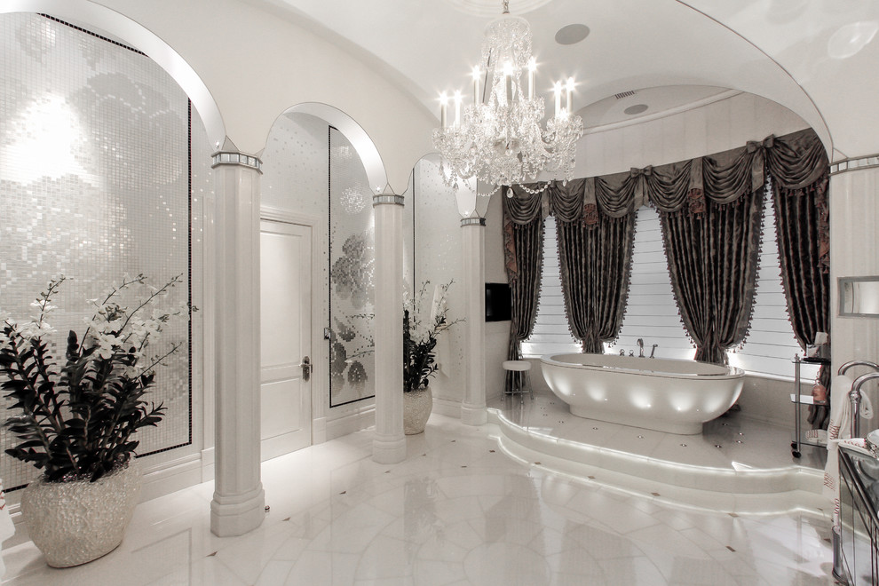 Пример оригинального дизайна: огромная главная ванная комната в стиле неоклассика (современная классика) с стеклянными фасадами, искусственно-состаренными фасадами, отдельно стоящей ванной, душевой комнатой, инсталляцией, белой плиткой, плиткой из листового камня, белыми стенами, мраморным полом, настольной раковиной, стеклянной столешницей, белым полом, душем с распашными дверями и разноцветной столешницей