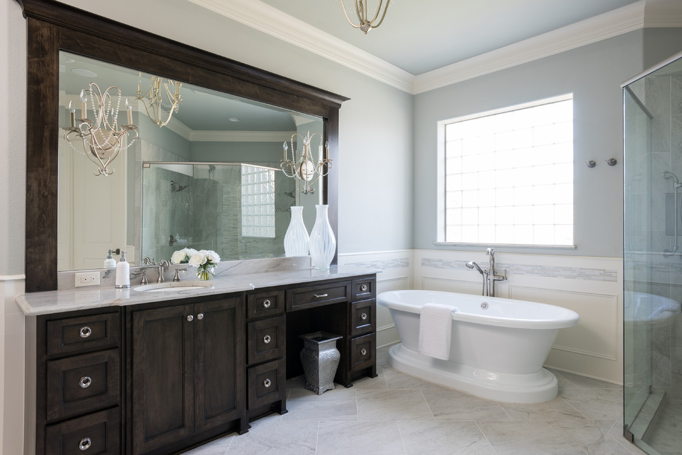 This is an example of a large traditional ensuite bathroom in Dallas with dark wood cabinets, a freestanding bath, a built-in shower, grey walls, porcelain flooring, a submerged sink, shaker cabinets, grey tiles, ceramic tiles, marble worktops, white floors and a hinged door.