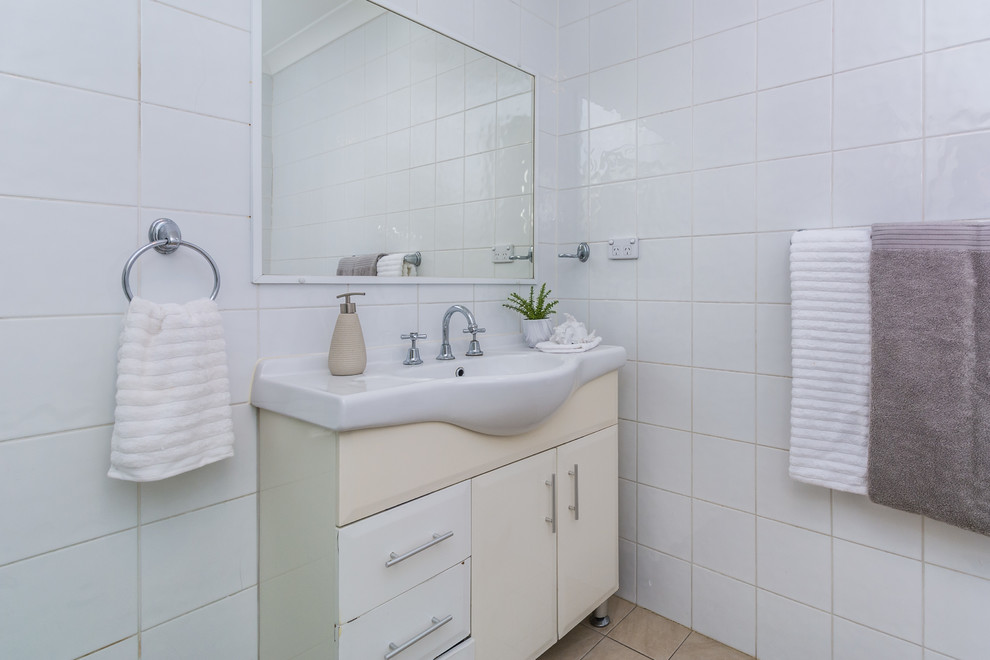 Réalisation d'une salle de bain design avec des portes de placard blanches, un carrelage blanc, des carreaux de porcelaine, un sol en carrelage de céramique, un lavabo posé et un sol beige.