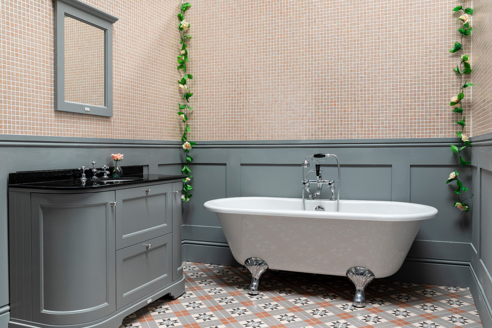 Пример оригинального дизайна: большая ванная комната в классическом стиле с фасадами островного типа, серыми фасадами, отдельно стоящей ванной, розовой плиткой, плиткой мозаикой, серыми стенами, полом из керамогранита, мраморной столешницей, разноцветным полом и черной столешницей