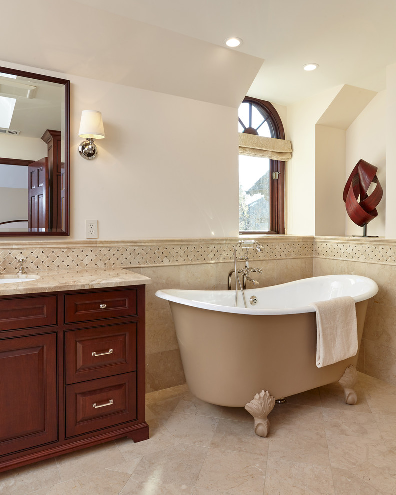 Cette image montre une grande salle de bain principale traditionnelle en bois foncé avec une baignoire sur pieds, un lavabo encastré, un carrelage beige, un mur beige, un sol beige, un placard à porte affleurante et un sol en marbre.