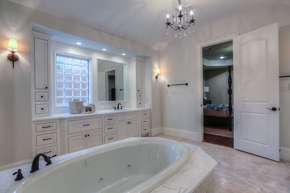 This is an example of a medium sized classic ensuite bathroom in Houston with a submerged sink, freestanding cabinets, white cabinets, granite worktops, a hot tub, a double shower, a one-piece toilet, beige tiles, grey walls and travertine flooring.