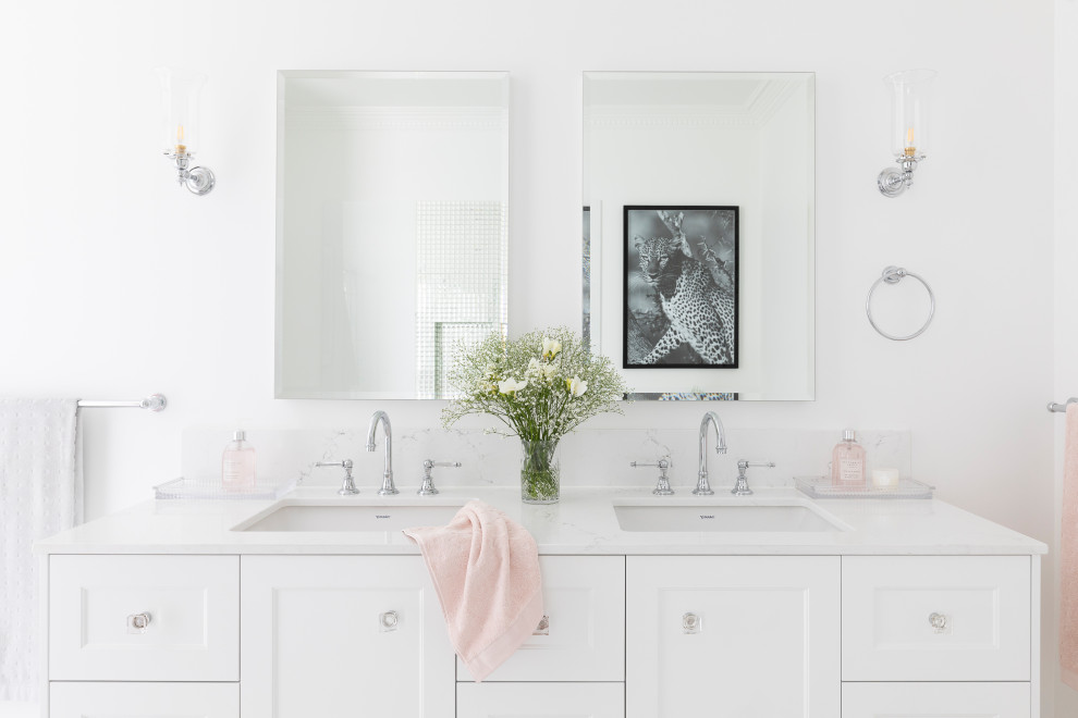 На фото: большая главная ванная комната в стиле неоклассика (современная классика) с фасадами в стиле шейкер, белыми фасадами, отдельно стоящей ванной, открытым душем, унитазом-моноблоком, белой плиткой, керамогранитной плиткой, белыми стенами, полом из керамической плитки, врезной раковиной, столешницей из искусственного кварца, розовым полом, душем с раздвижными дверями, белой столешницей, тумбой под две раковины и встроенной тумбой с