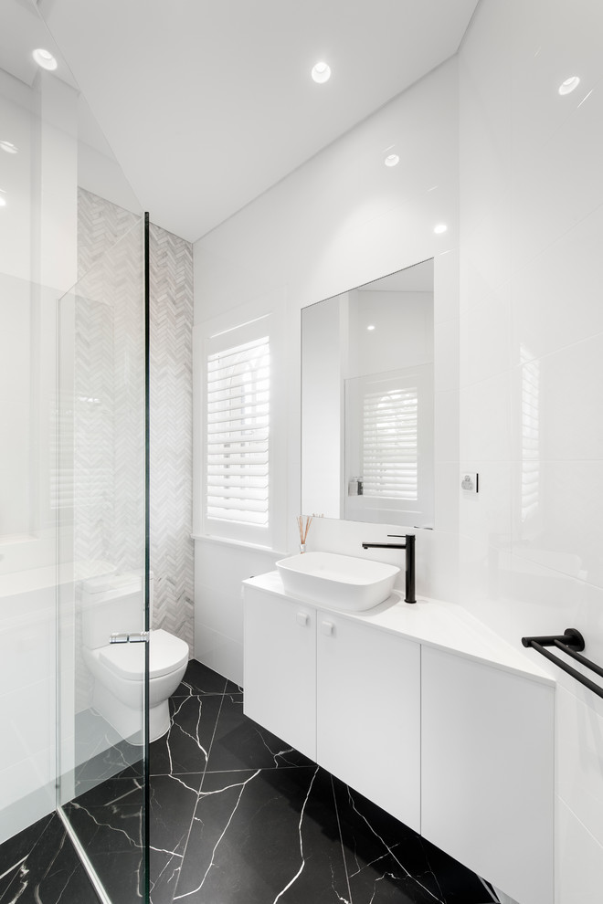 Inspiration for a large contemporary ensuite bathroom in Adelaide with flat-panel cabinets, white cabinets, a one-piece toilet, white tiles, marble tiles, white walls, marble flooring, a vessel sink, engineered stone worktops, black floors, a corner shower and a hinged door.