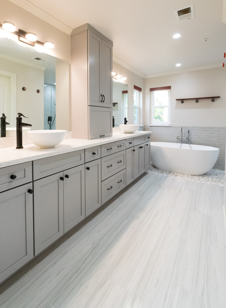 This is an example of a large modern ensuite bathroom in San Francisco with shaker cabinets, grey cabinets, a freestanding bath, a built-in shower, a one-piece toilet, grey tiles, ceramic tiles, grey walls, ceramic flooring, a vessel sink, grey floors and a hinged door.