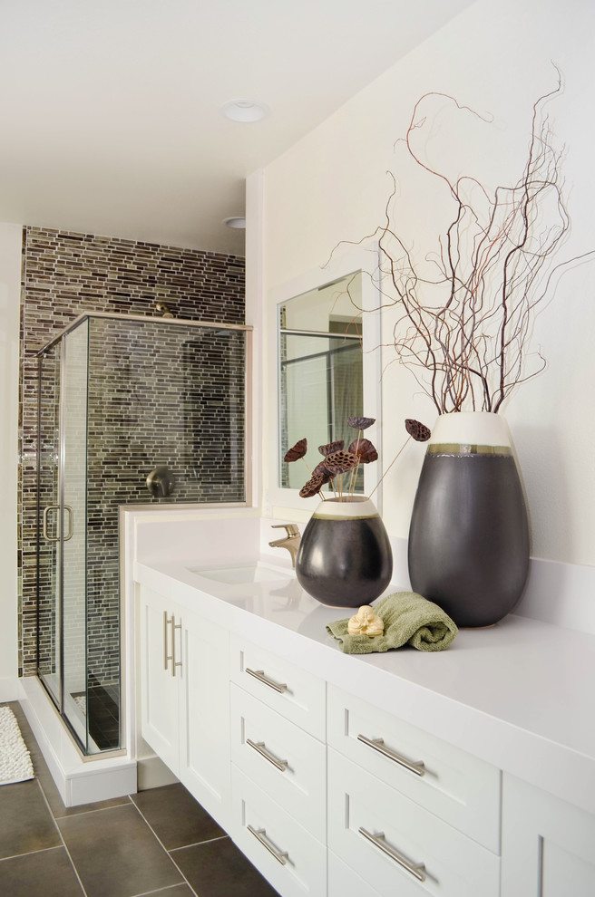 Photo of an expansive traditional ensuite bathroom in Los Angeles with shaker cabinets, white cabinets, a freestanding bath, an alcove shower, a one-piece toilet, grey tiles, glass sheet walls, white walls, porcelain flooring, a submerged sink, solid surface worktops, grey floors, a hinged door and white worktops.