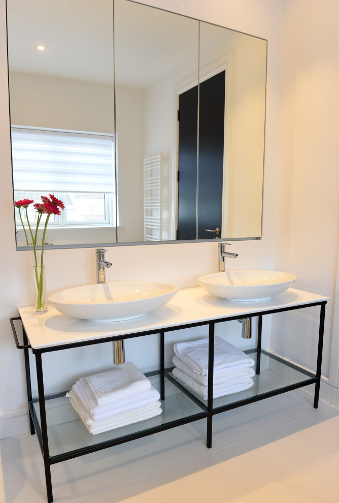 Inspiration for a large modern ensuite bathroom in Dublin with open cabinets, white cabinets, a freestanding bath, an alcove shower, a wall mounted toilet, white tiles, mirror tiles, black walls, porcelain flooring, a vessel sink, solid surface worktops, white floors, a sliding door, white worktops, a wall niche, double sinks and a built in vanity unit.