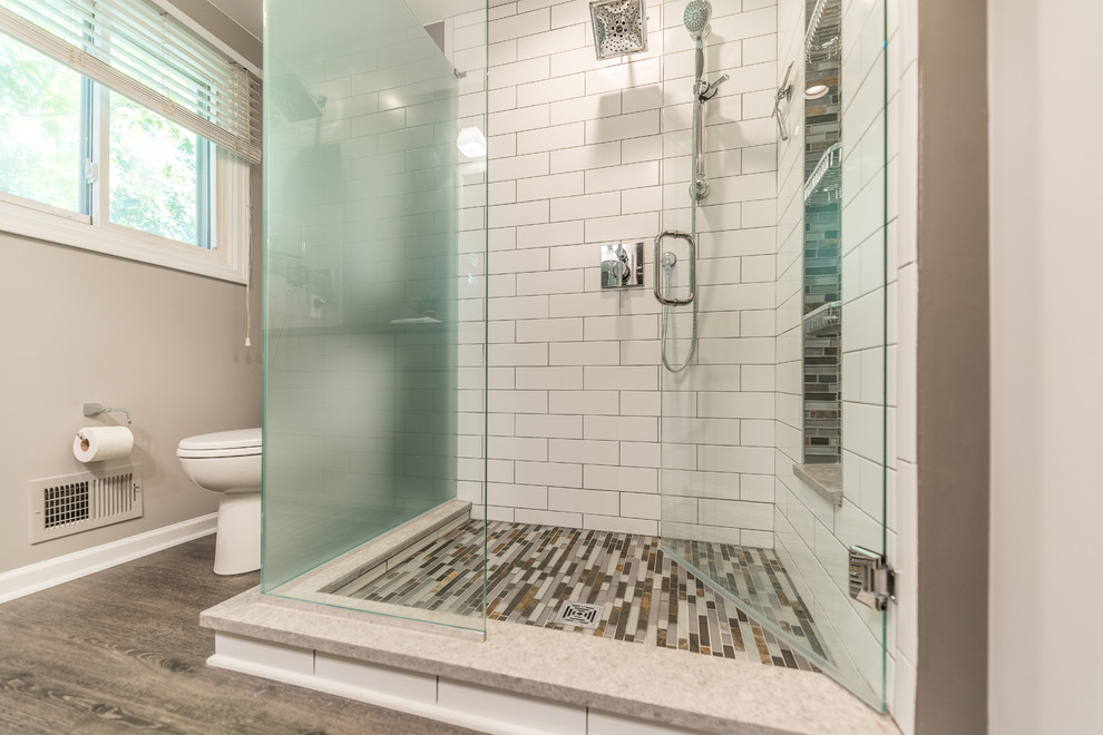 Inspiration for a medium sized contemporary ensuite bathroom in Detroit with flat-panel cabinets, grey cabinets, a corner shower, a two-piece toilet, white tiles, glass sheet walls, grey walls, vinyl flooring, a submerged sink, glass worktops, multi-coloured floors, a hinged door and grey worktops.