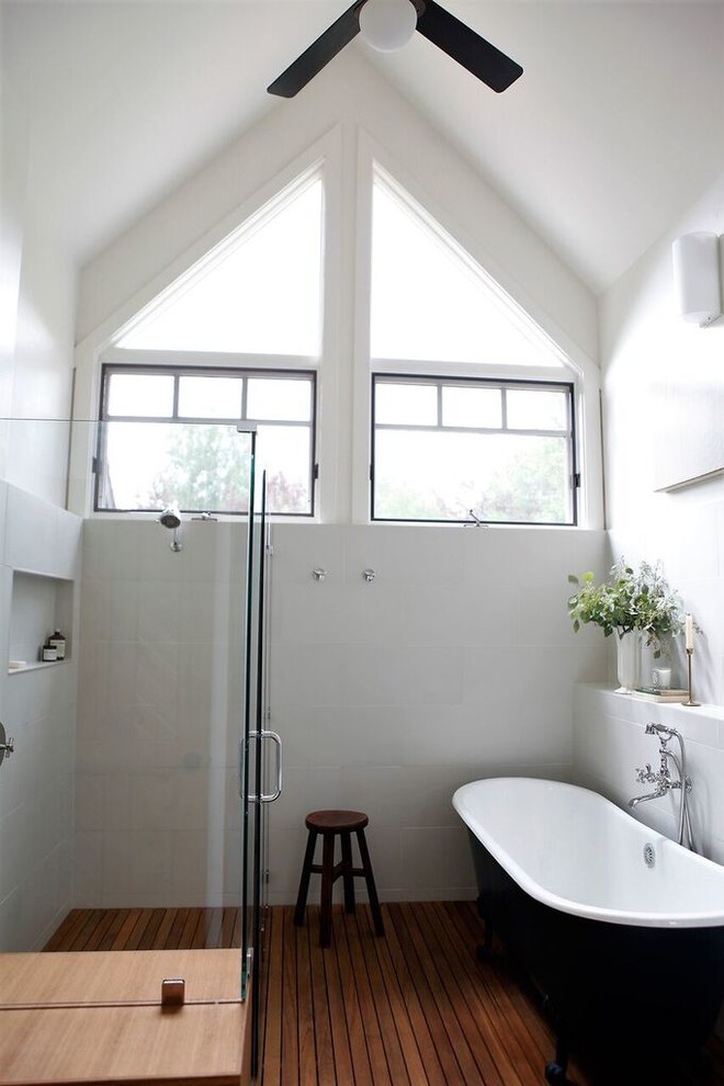 Réalisation d'une salle de bain principale design avec une baignoire sur pieds, un carrelage blanc, des carreaux de céramique, un mur blanc, un sol en bois brun, un sol marron et un plafond voûté.
