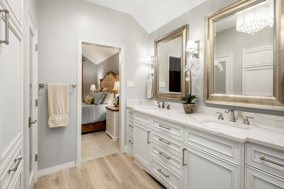 Corner shower - mid-sized transitional master gray tile and marble tile porcelain tile and brown floor corner shower idea in Dallas with recessed-panel cabinets, white cabinets, a two-piece toilet, gray walls, an undermount sink, quartz countertops, a hinged shower door and white countertops