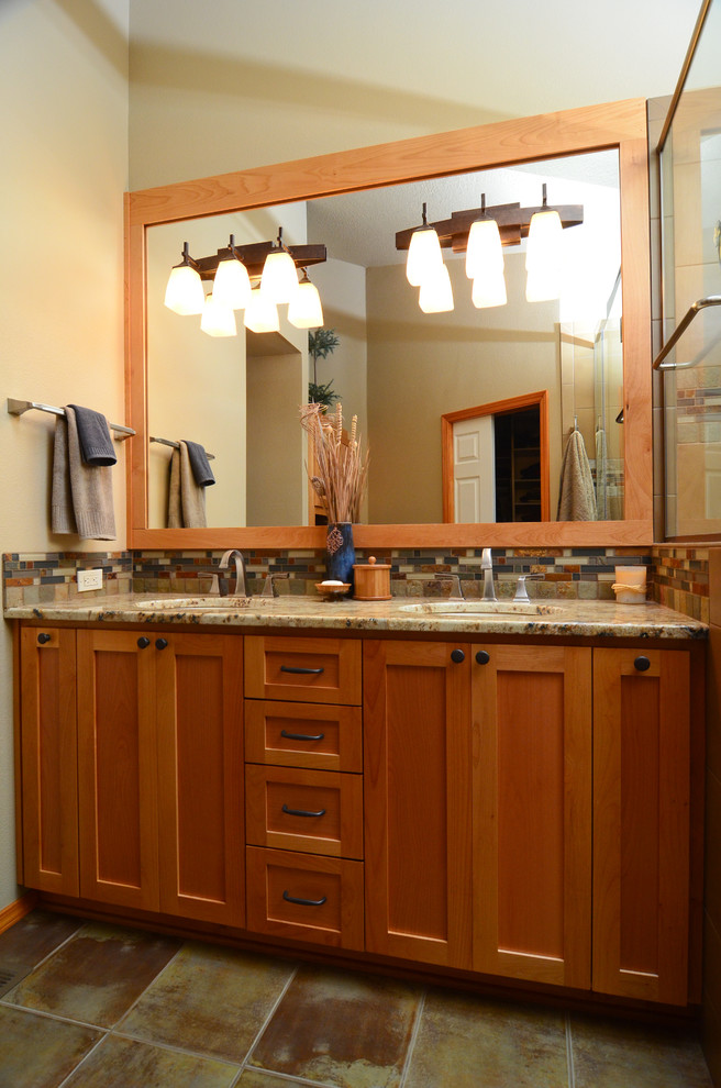 Inredning av ett amerikanskt badrum, med ett undermonterad handfat, skåp i shakerstil, skåp i mellenmörkt trä, granitbänkskiva, en dusch i en alkov, flerfärgad kakel och beige väggar
