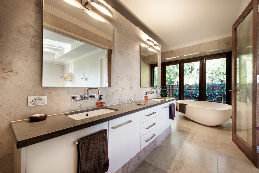 Ispirazione per una stanza da bagno padronale minimal con lavabo sottopiano, ante lisce, ante bianche, vasca freestanding e piastrelle grigie